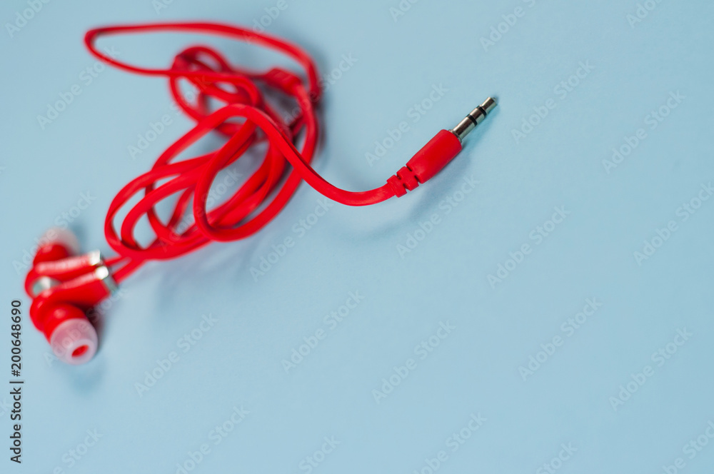 Red new earphone with cable and metal plug on blue paper background with copy space Red new earphone with cable and metal plug on blue paper background with copy space