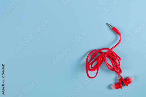 Red new earphone with cable and metal plug on blue paper background with copy space