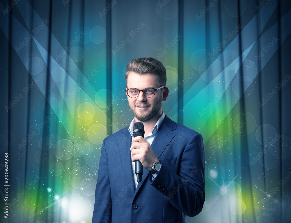 Businessman speaking into microphone with blue curtain behind him Businessman speaking into microphone with blue curtain behind him