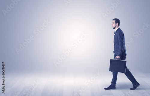 Successful businessman walking in front of an empty wall with briefcase on his hand
