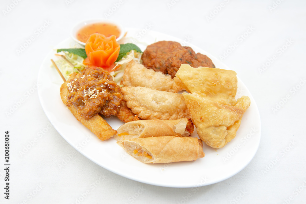 Mixture of Thai appertizers with deep-fried spring rolls, curry puffs, wontons, fish cakes and chicken satay skewers Mixture of Thai appertizers with deep-fried spring rolls, curry puffs, wontons, fish cakes and chicken satay skewers