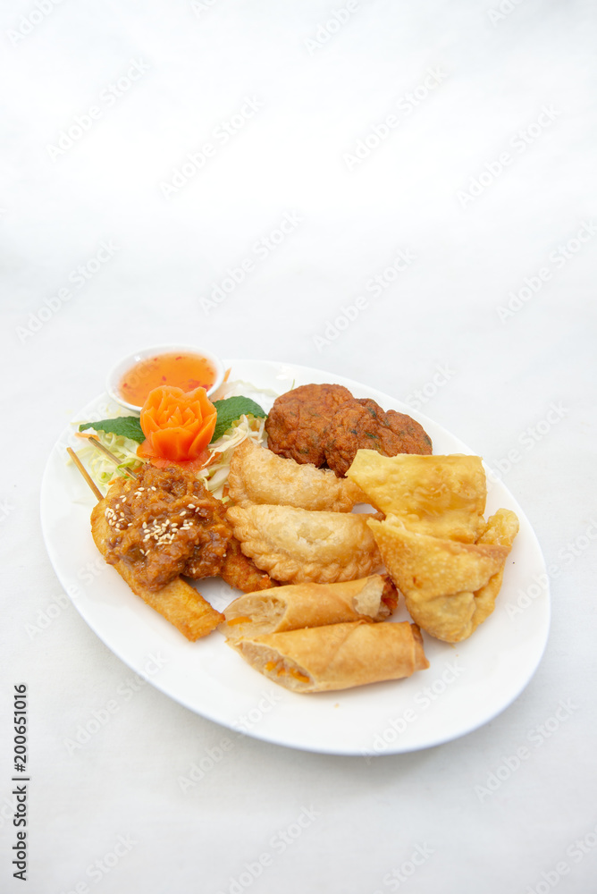 Mixture of Thai appertizers with deep-fried spring rolls, curry puffs, wontons, fish cakes and chicken satay skewers Mixture of Thai appertizers with deep-fried spring rolls, curry puffs, wontons, fish cakes and chicken satay skewers
