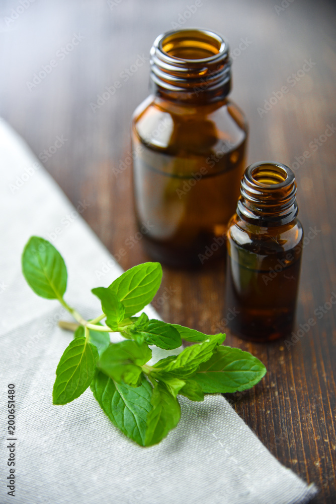 Essential oil of peppermint in a small brown bottle with fresh green mint on an old wooden background, selective focus Essential oil of peppermint in a small brown bottle with fresh green mint on an old wooden background, selective focus