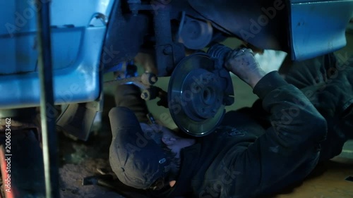 The mechanic in dirty auto repair shop repairs the car - repairs constant-velocity universal ball joint Shrus and replaces a wheel photo