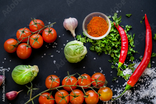 Close up of colorful spices and fresh vegetables for cooking on dark metal background with space for text. Top view. Bio Healthy food ingredients.