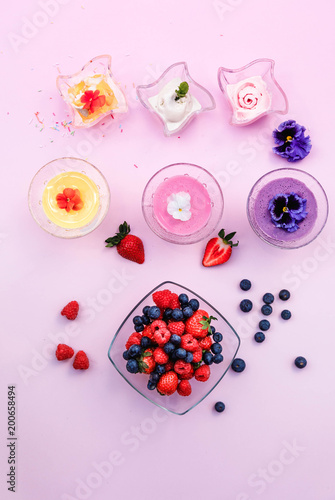 Ice cream in wave glass bowls and creamy milk beverage, smoothie with edible flowers *pansy, violet (on pink background. Pink (strawberry), yellow (mango or banana) Top view