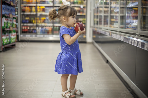 Little girl eating apple in the supermarket