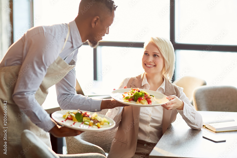 Happy young manager taking plate with her order in cafe and saying thanks to waiter Happy young manager taking plate with her order in cafe and saying thanks to waiter