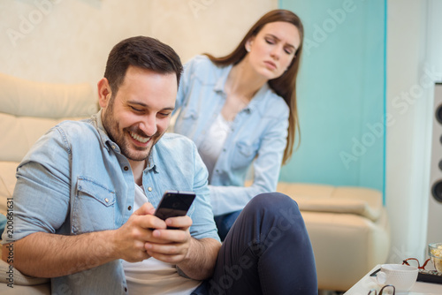 Fotografie Jealous woman spying her husband smart phone