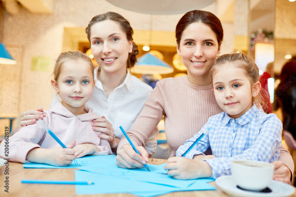 Pretty females and their little daughters drawing with blue highlighters while spending leisure in cafe