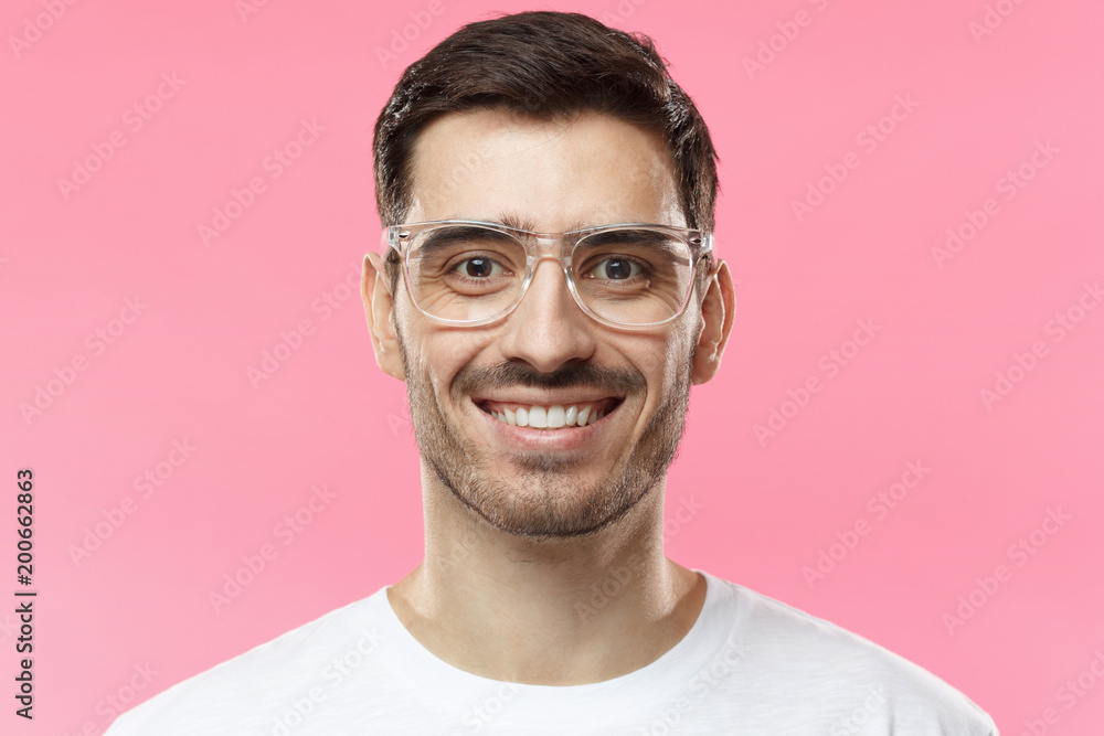 Close up portrait of smiling handsome man in trendy glasses and white t-shirt isolated on pink background Close up portrait of smiling handsome man in trendy glasses and white t-shirt isolated on pink background
