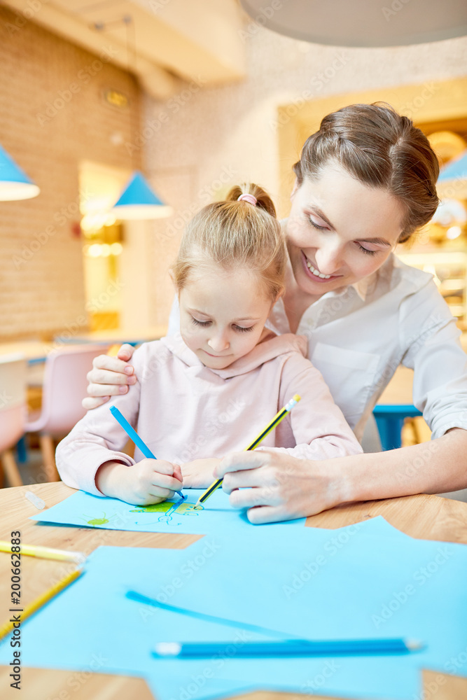 Fototapeta premium Young mother helping her daughter to draw while spending leisure in cafe