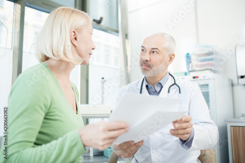 Confident clinician and his patient discussing medical papers or prescriptions during appointment