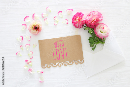 Image of envelope with delicate pastel pink beautiful flowers arrangement over white wooden background. Flat lay  top view.