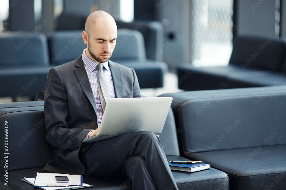 Serious businessman browsing in the net while waiting for departure in airport lounge Serious businessman browsing in the net while waiting for departure in airport lounge