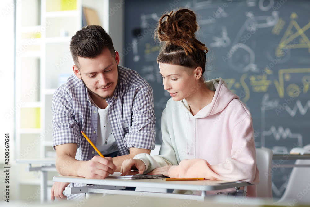 Clever guy and girl discussing lecture notes in copybook while preparing for seminar in classroom at break Clever guy and girl discussing lecture notes in copybook while preparing for seminar in classroom at break