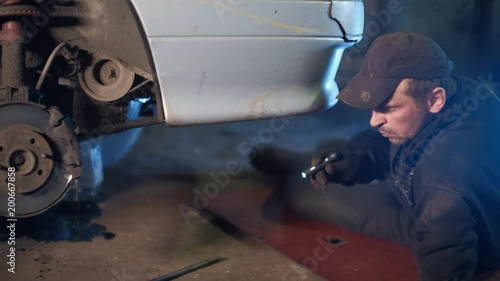 The mechanic in dirty auto repair shop repairs the car - repairs constant-velocity universal ball joint Shrus and replaces a wheel photo