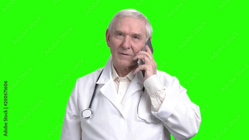 Old smiling doctor talking on the phone. Portrait of old doctor using smartphone in green hroma background. Old smiling doctor talking on the phone. Portrait of old doctor using smartphone in green hroma background.