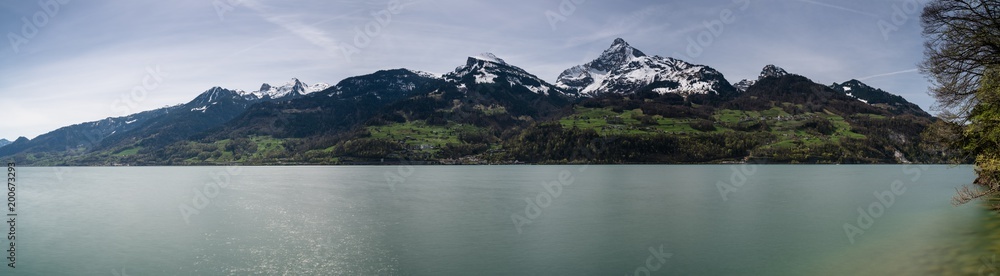 panorama view of a beautiful turquoise mountain lake panorama with snow-covered peaks and green meadows and forests panorama view of a beautiful turquoise mountain lake panorama with snow-covered peaks and green meadows and forests