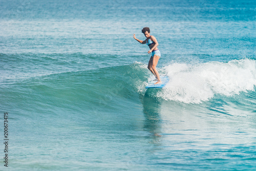 Pacific islander melanesian papuan surfer girl with afro surfing on blue longboard in crystal clear water at Padang Padang beach, Bali, Indonesia