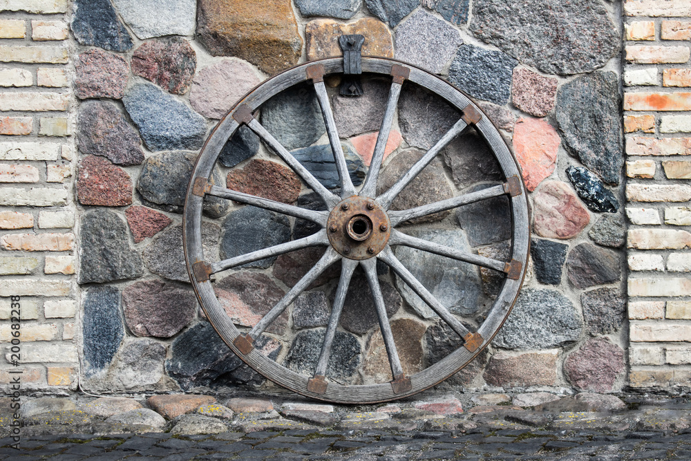 Large ancient wooden cart wheel attached to the wall made of stones.