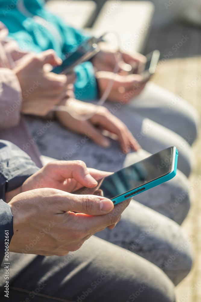Obraz premium A group of hipster friends sitting on the street holding smartphones in their hands. Young people, students use phones for online communication.