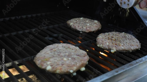 chef seasoning fresh hamburger patties on the grill