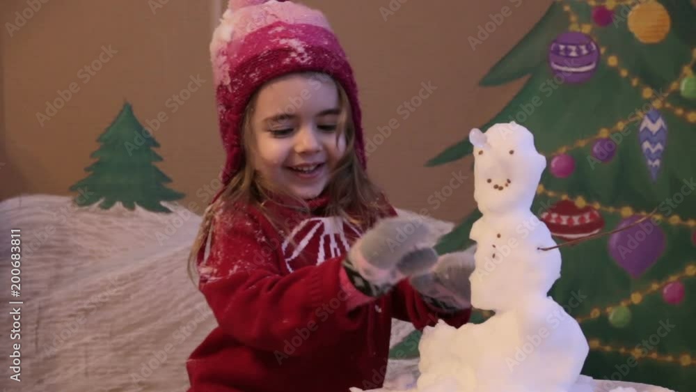 Girl sculpts a snowman in winter. Emotional portrait of cute little girl in winter. background of a painted Christmas tree and snow Girl sculpts a snowman in winter. Emotional portrait of cute little girl in winter. background of a painted Christmas tree and snow
