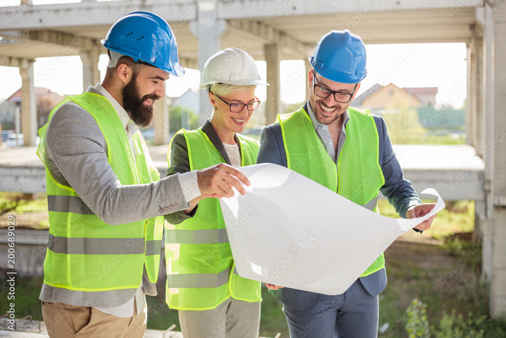 Mixed group of smiling engineers or business partners at construction site, working together on building's blueprint. Architecture and teamwork concept.