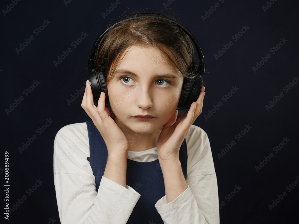 Girl with headphones, looking away from camera, dark background, serious face. Girl with headphones, looking away from camera, dark background, serious face.
