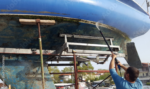 Man cleaning the bottom of a sailboat with high pressure water