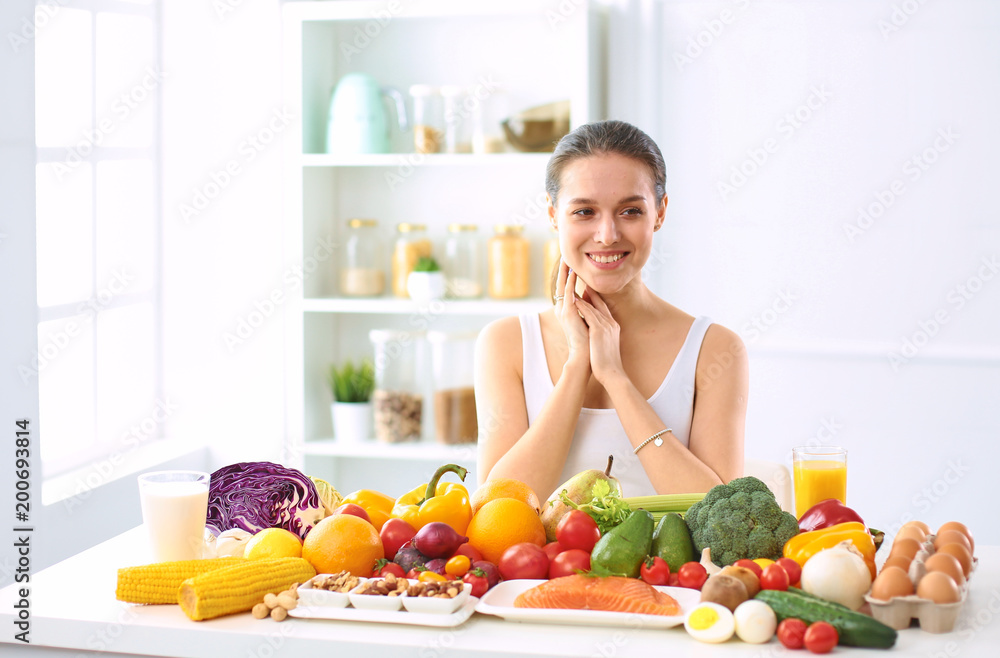 happy young housewife sitting in the kitchen preparing food from a pile of diverse fresh organic fruits and vegetables happy young housewife sitting in the kitchen preparing food from a pile of diverse fresh organic fruits and vegetables