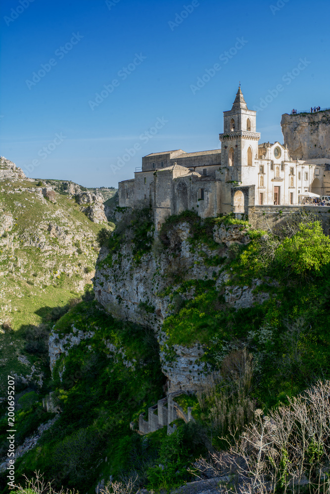 Vertical View of the Church of Peter and Paul Saints on the Background of the Caves of the Gravina of Matera on Blue Sky Background. Matera, South of Italy