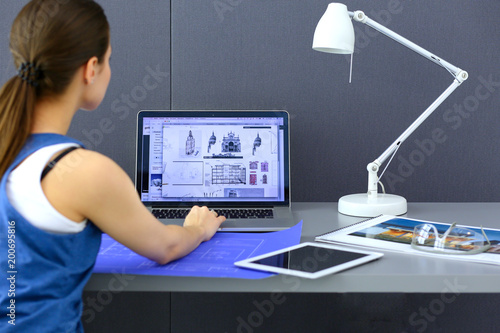 Young woman sitting at the desk with instruments, plan and laptop photo