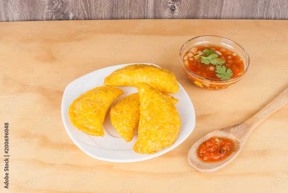 Colombian empanada with spicy sauce on wooden background Colombian empanada with spicy sauce on wooden background