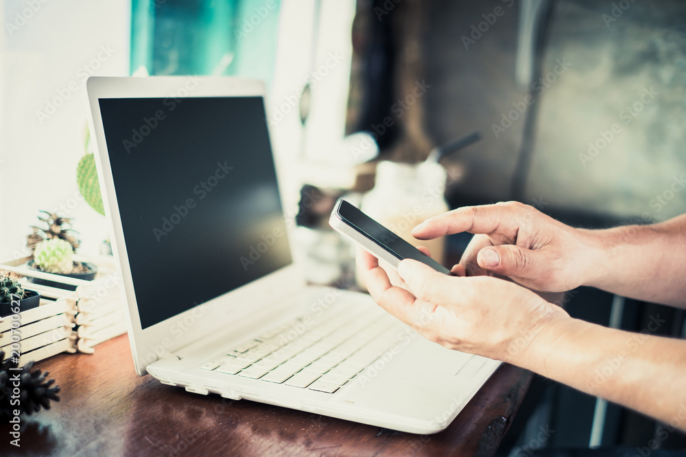 Businessman using smartphone and laptop writing on wooden table in coffee shop with a cup of coffee Businessman using smartphone and laptop writing on wooden table in coffee shop with a cup of coffee