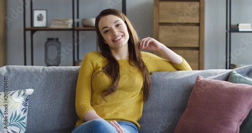 Portrait shot of the brunette attractuve woman looking in the camera and smiling while sitting on the cozy couch in the living room. Portrait shot. Indoors photo
