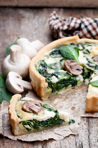 Traditional french quiche pie with spinach and mushroom on wooden table