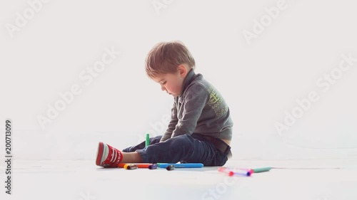 little boy draws colored pencils on paper in a white room photo