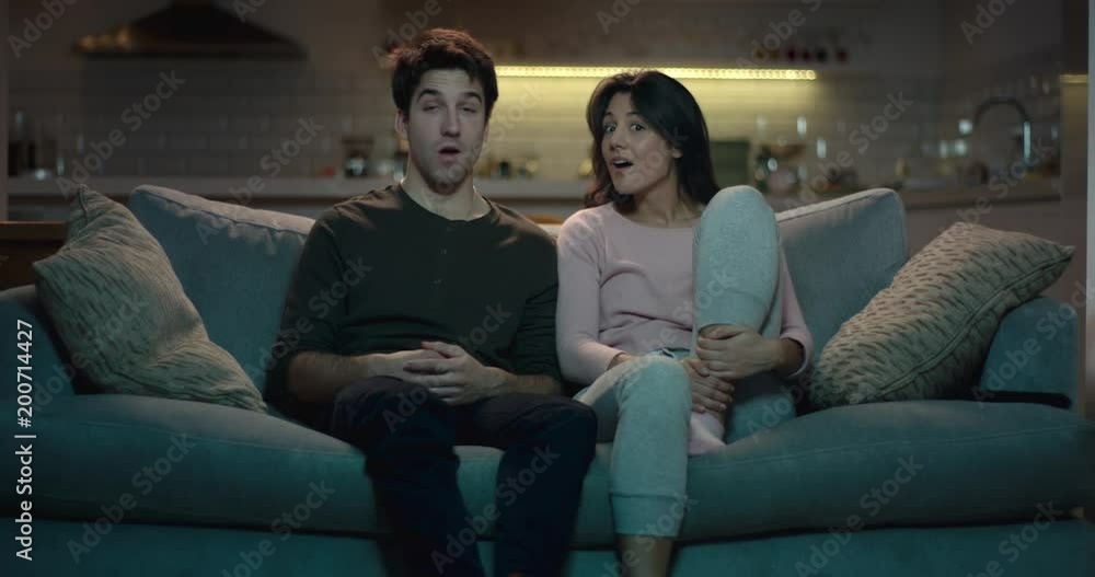 Man and woman watching tv with shocked expressions on their faces. Man and woman watching tv with shocked expressions on their faces.