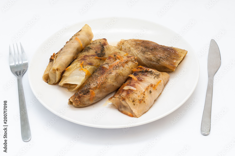 Tasty stuffed cabbage leaf laying on plate on isolated white background, fork and knife on both sides Tasty stuffed cabbage leaf laying on plate on isolated white background, fork and knife on both sides