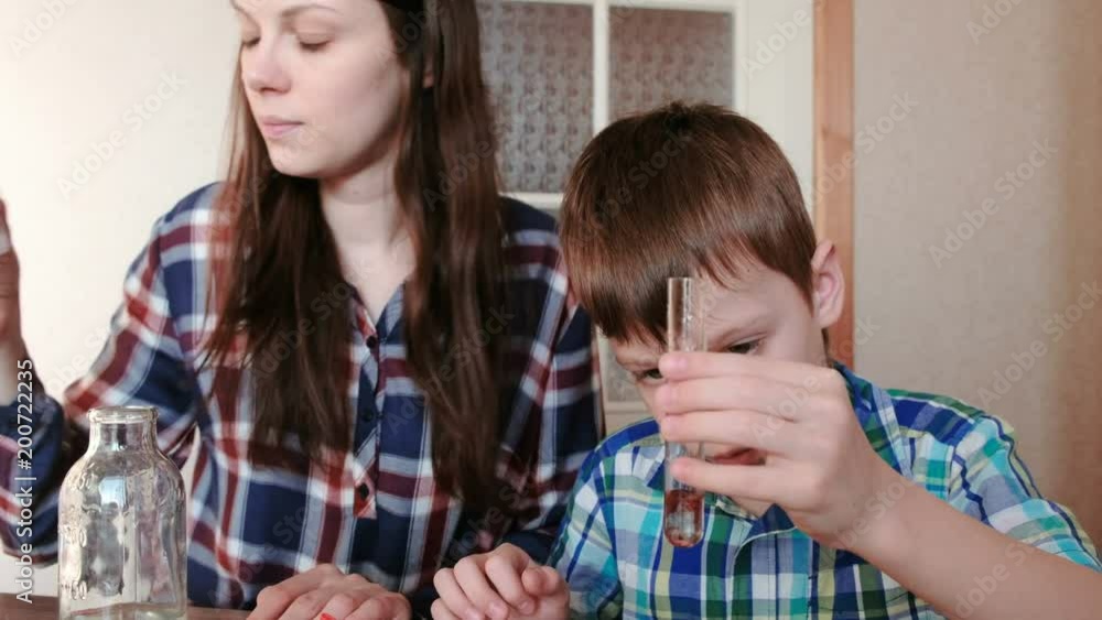 Chemistry experiments at home. Woman puts the red paint in a test tube with water in the hands of the boy. Chemistry experiments at home. Woman puts the red paint in a test tube with water in the hands of the boy.