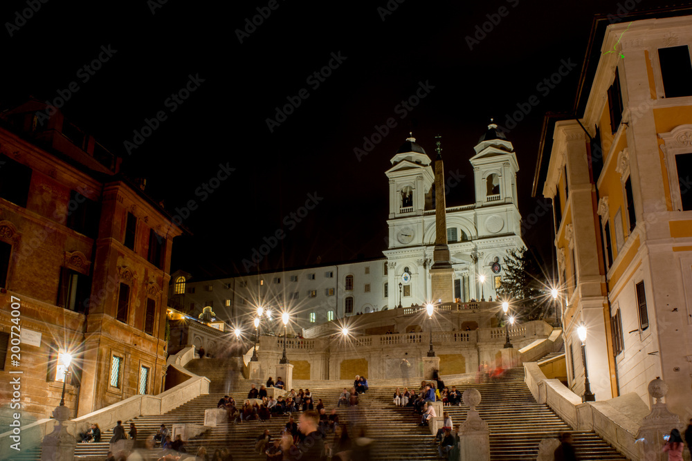 Horizontal View of a Square Called Piazza di Spagna at Night with Blur People and the Flight of Steps of The Church Called Trinità dei Monti Illuminated by Artificial Lights. Rome, Italy