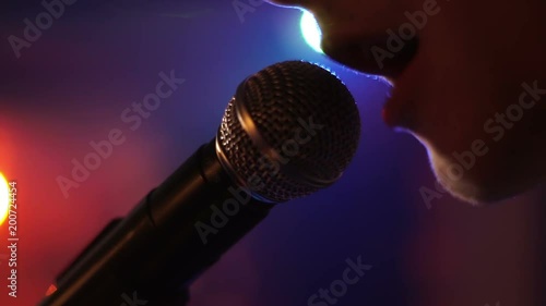 Man singing song in microphone during performance on stage on rock concert. Close up man rock star singer on music concert on colorful light background.