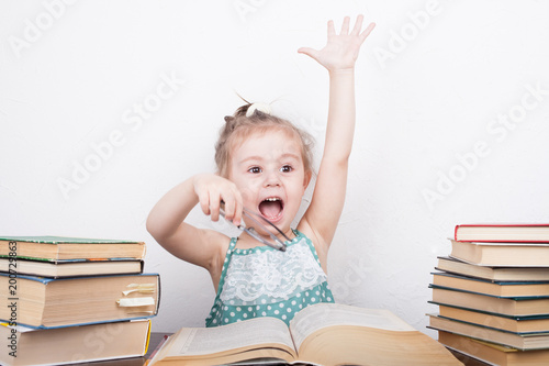 Beautiful little girl is sitting at the table with a bunch of books photo