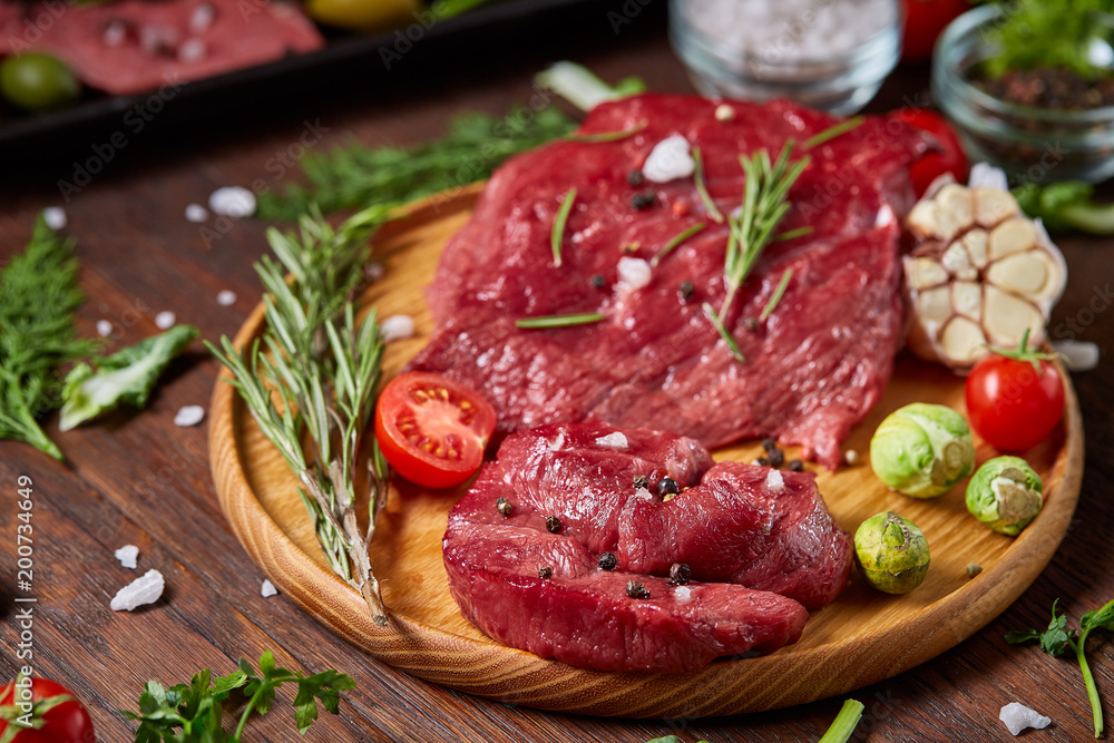 Still life of raw beef meat with vegetables on wooden plate over white background, top view, selective focus