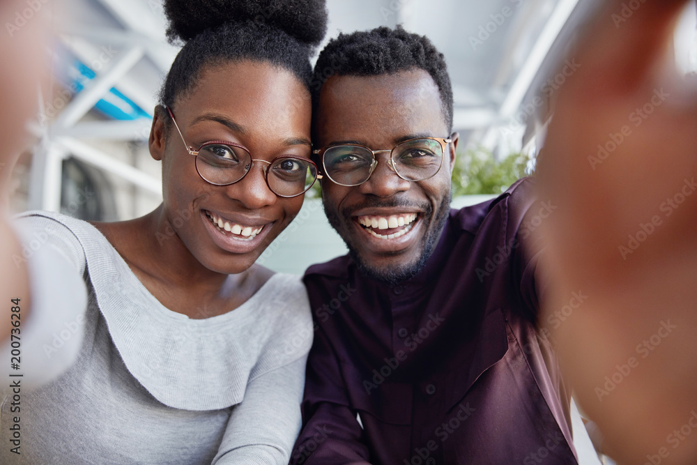 Glad African friends enjoy resting together, have positive expressions, make photo, stretch hand as take selfie, share pictures in social networks. African American woman and man in spectacles Glad African friends enjoy resting together, have positive expressions, make photo, stretch hand as take selfie, share pictures in social networks. African American woman and man in spectacles