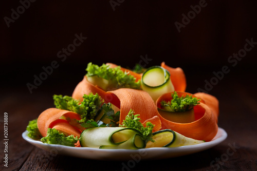 Artistically served vegetable salad with carrot, cucumber, letucce over wooden background, selective focus