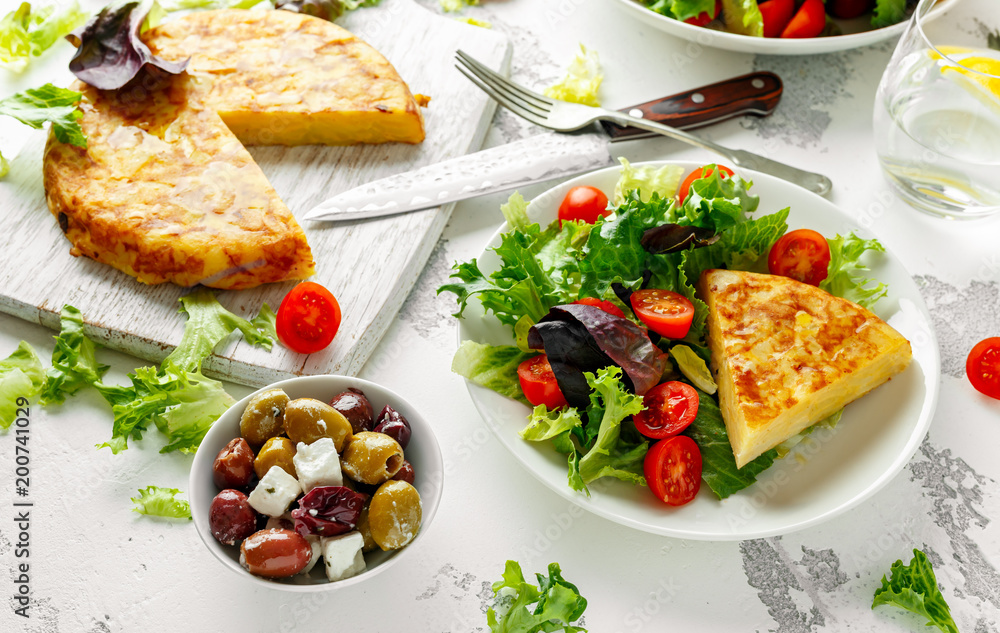 Spanish tortilla, omelette with potato, onion, vegetables, tomatoes, olives and herbs in a white plate. breakfast, healthy food.