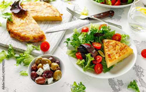 Spanish tortilla, omelette with potato, onion, vegetables, tomatoes, olives and herbs in a white plate. breakfast, healthy food.